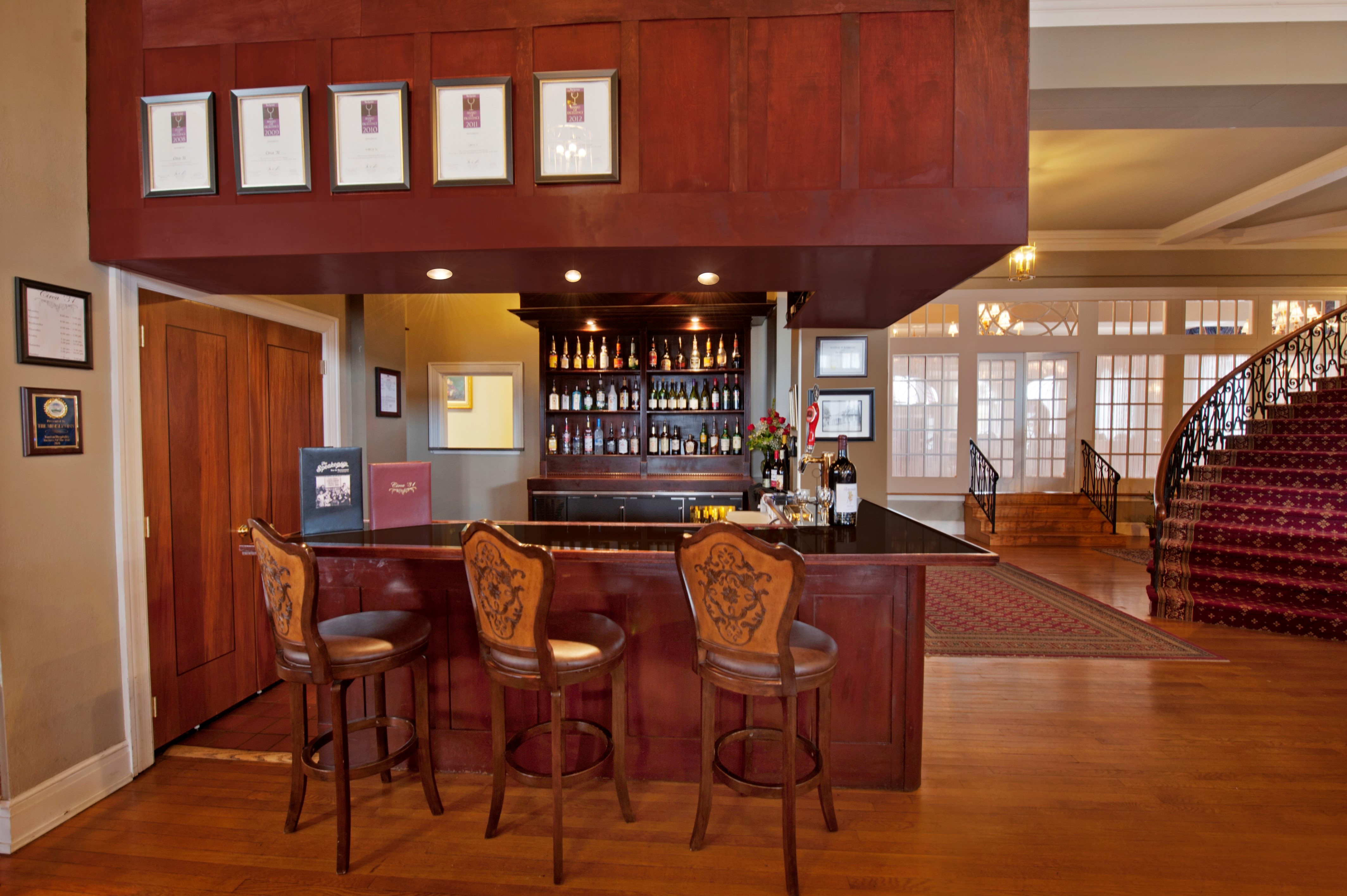 a bar with chairs in a room with a staircase and a rug