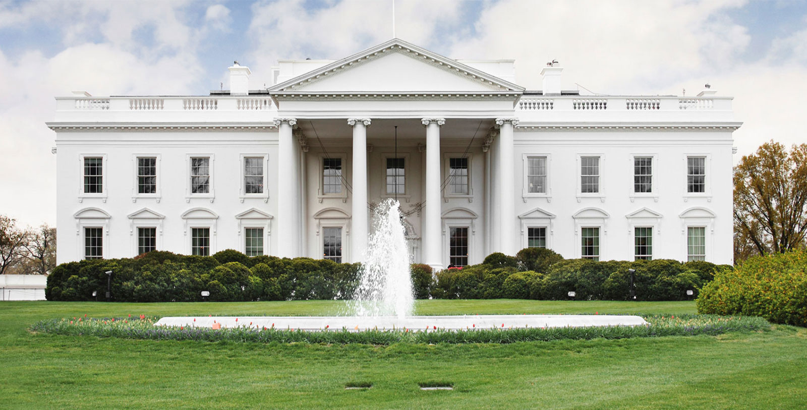 a white building with columns and a fountain in front of it with White House in the background