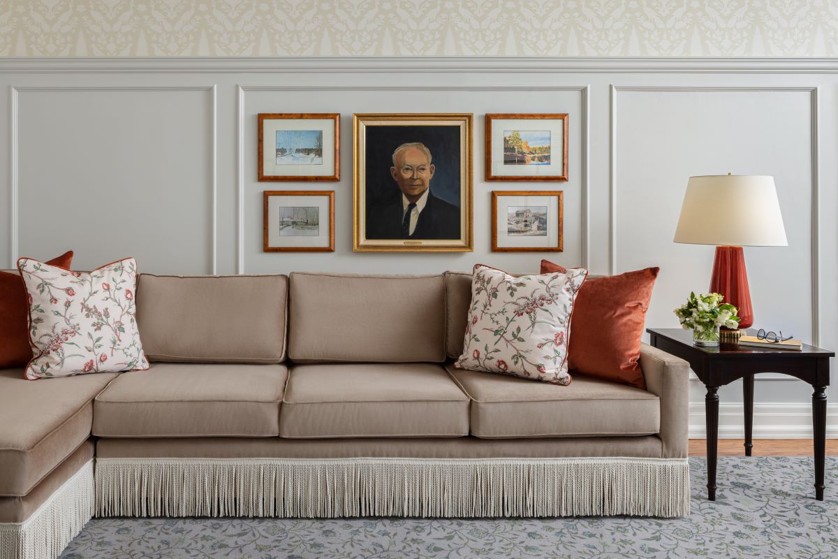 a couch with pillows in a room with a lamp and pictures on the wall