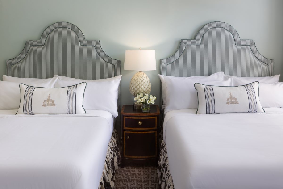 two beds with white sheets and a lamp on a nightstand