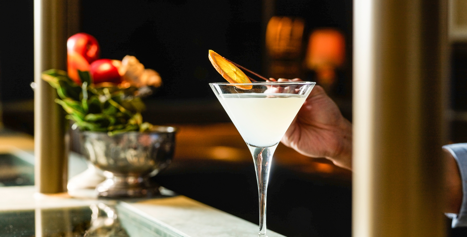 a hand holding a martini glass with a slice of orange on top