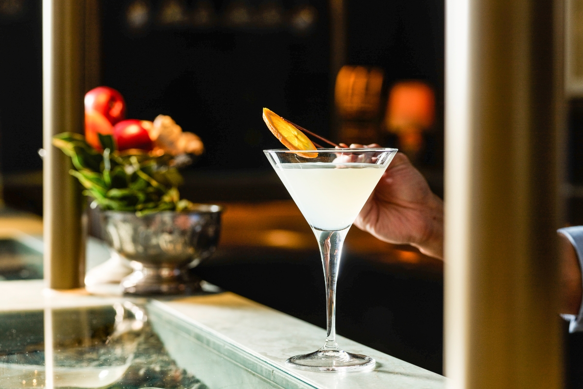a hand holding a martini glass with a slice of orange on top