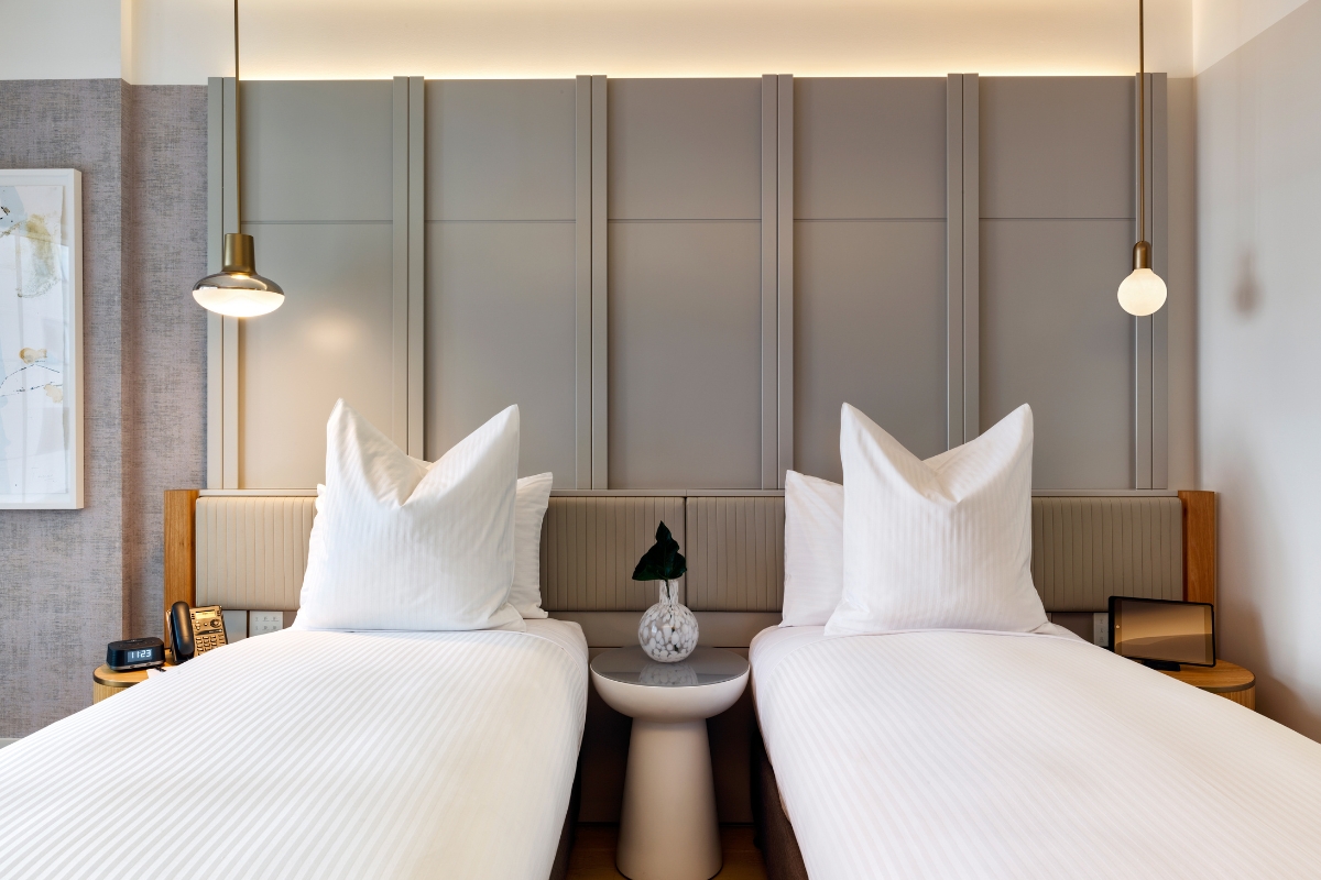 two beds with white sheets and a small table