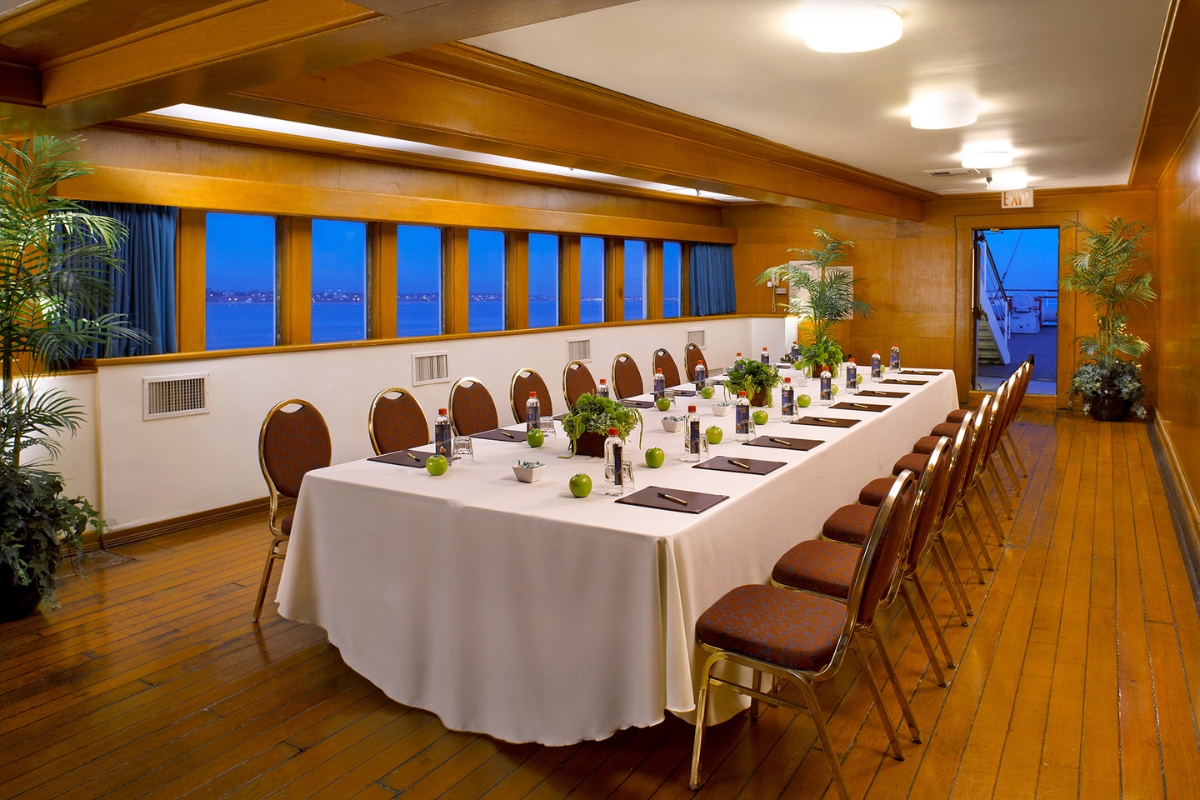 a long table with white tablecloths and chairs in a room with windows