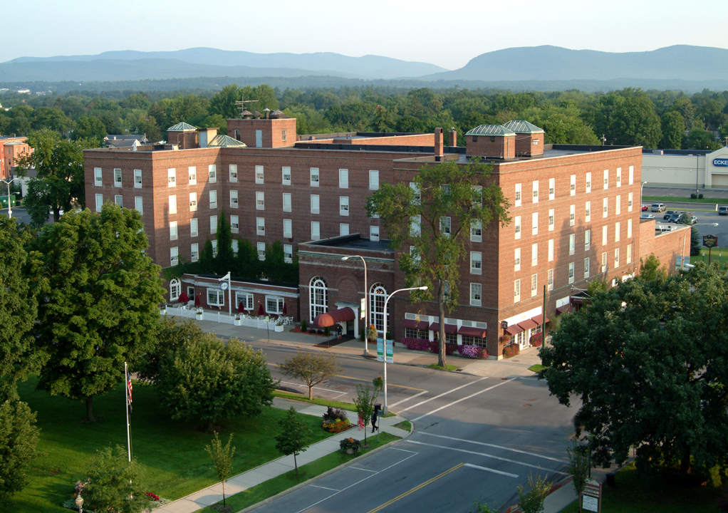 a large brick building with trees and mountains in the background