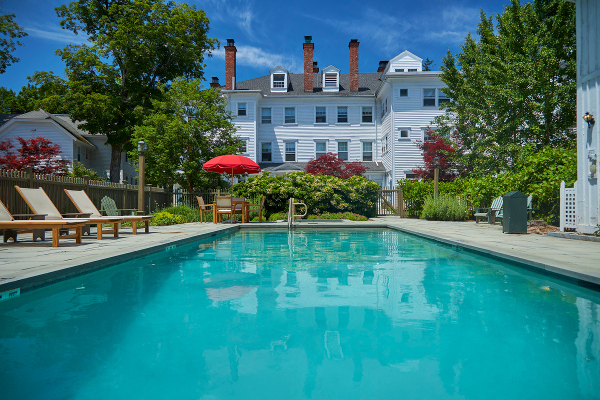 a pool with chairs and a red umbrella in front of a large white building