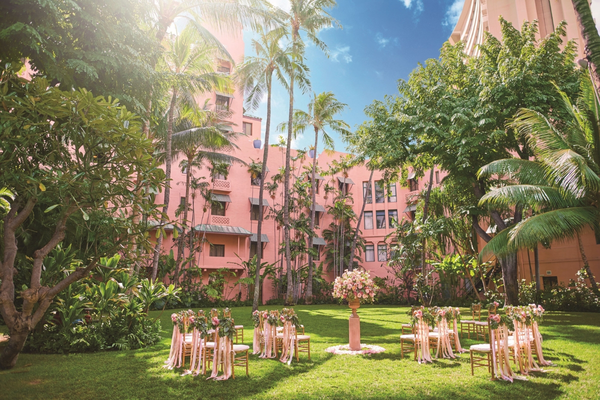 a pink building with palm trees and chairs in front of it
