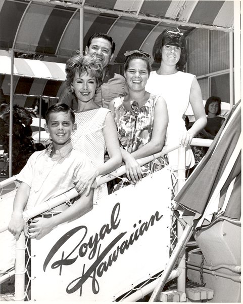 Vintage black-and-white photograph of a family posing together on a walkway outdoors in front of a sign that reads 'Royal Hawaiian' under a striped awning.