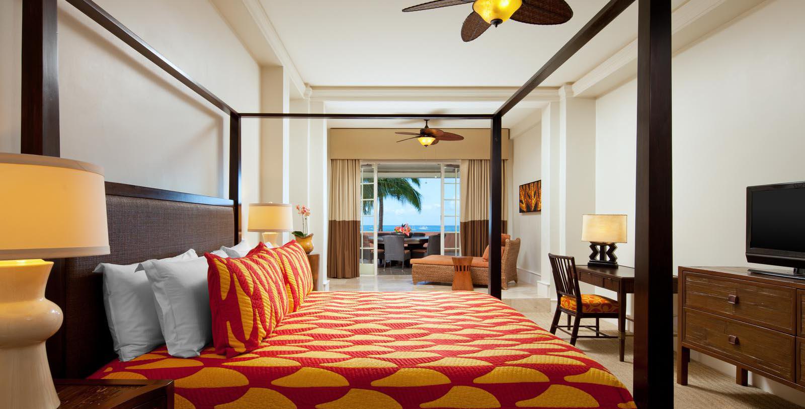 a bed with a four poster bed and a fan in a room with a view of the ocean