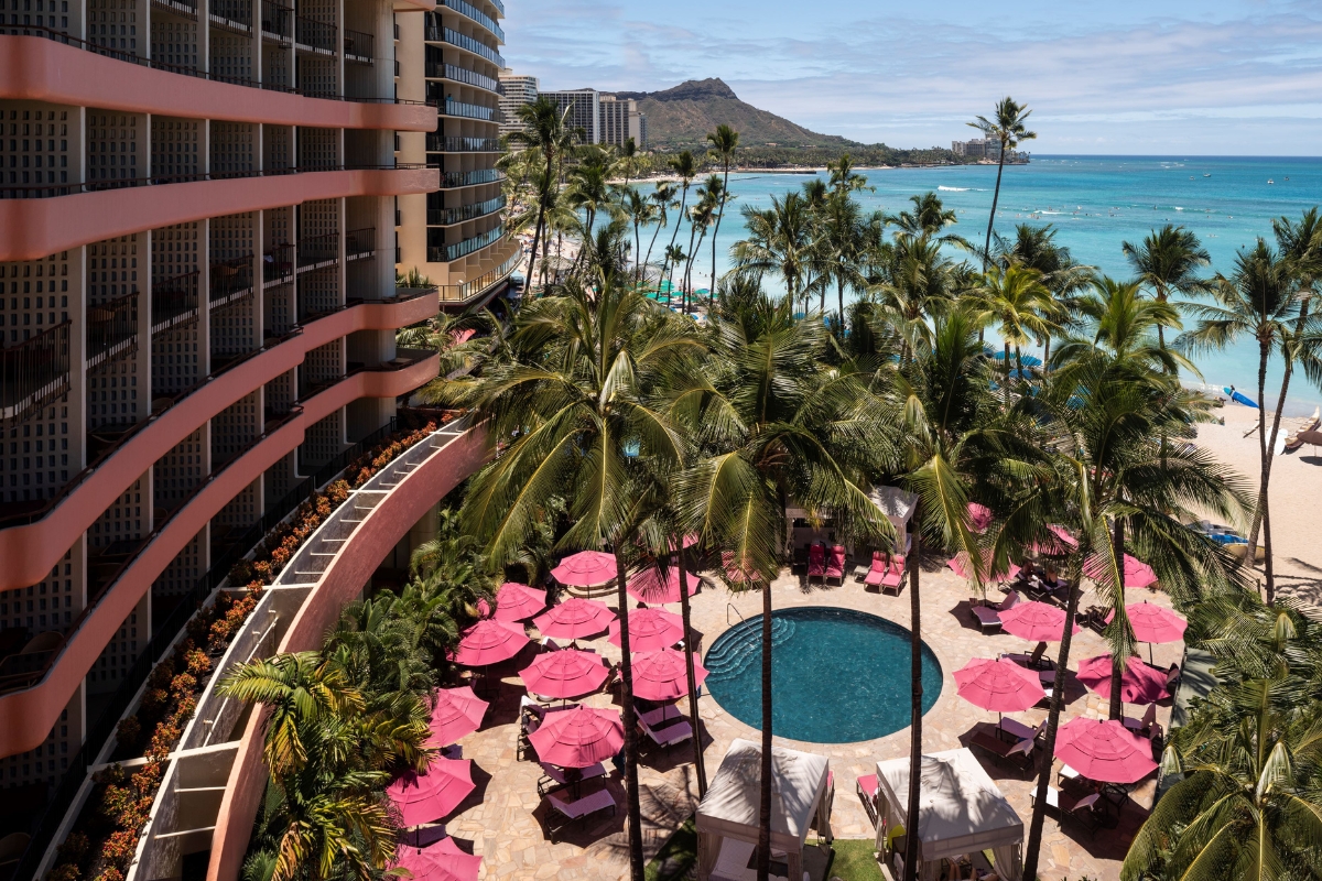 a pool with pink umbrellas and palm trees by a building