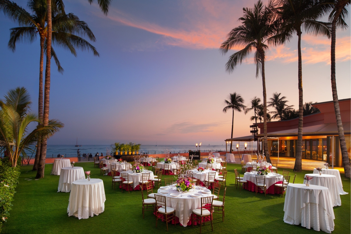 a group of tables set up on a lawn with palm trees and a building