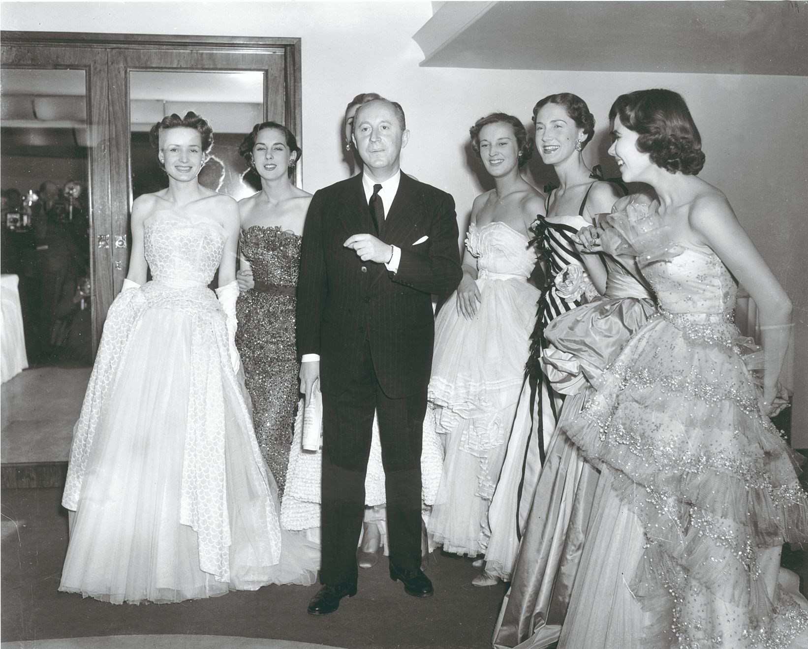 a man in a suit standing next to a group of women in dresses