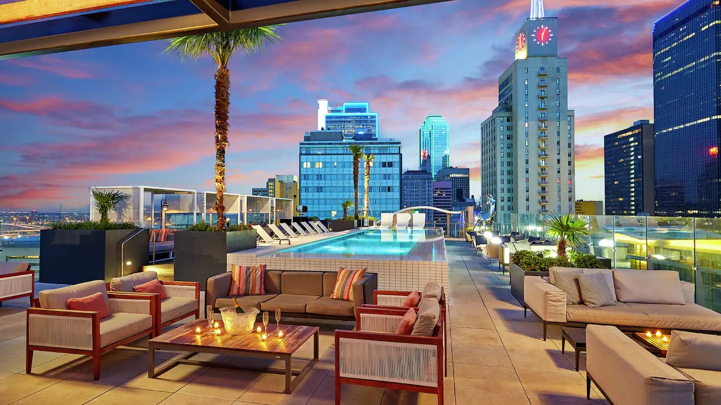 a rooftop patio with a pool and chairs and tables with a city skyline in the background
