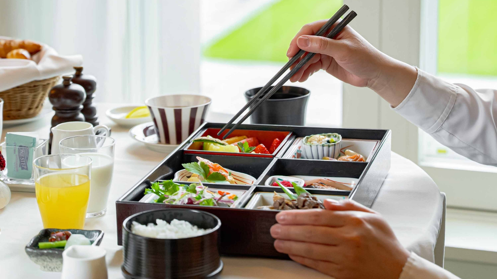 a person holding chopsticks over a rectangular box of food