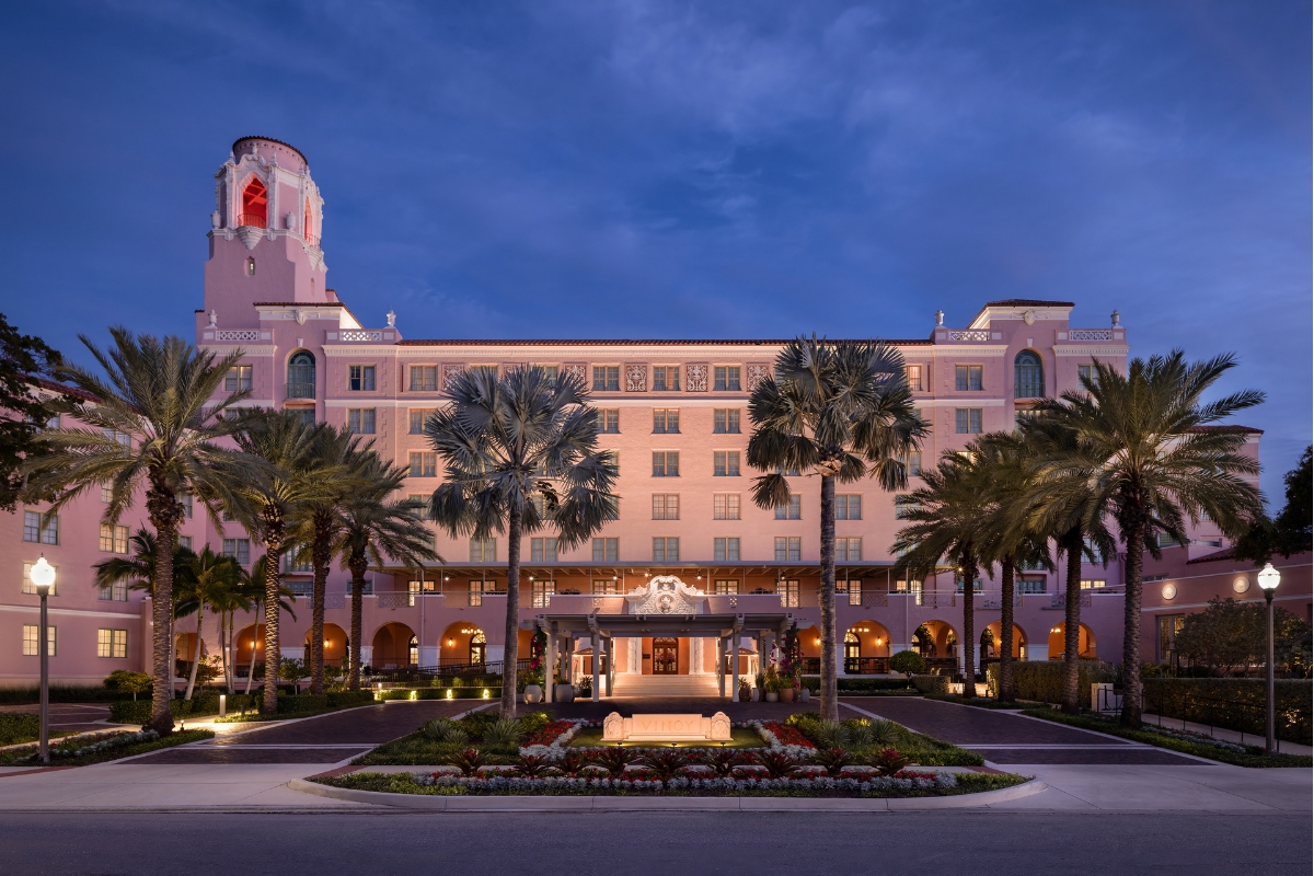 Exterior dusk view of The Vinoy resort, a grand Mediterranean Revival-style pink hotel illuminated against a twilight sky with palm trees along the front driveway.