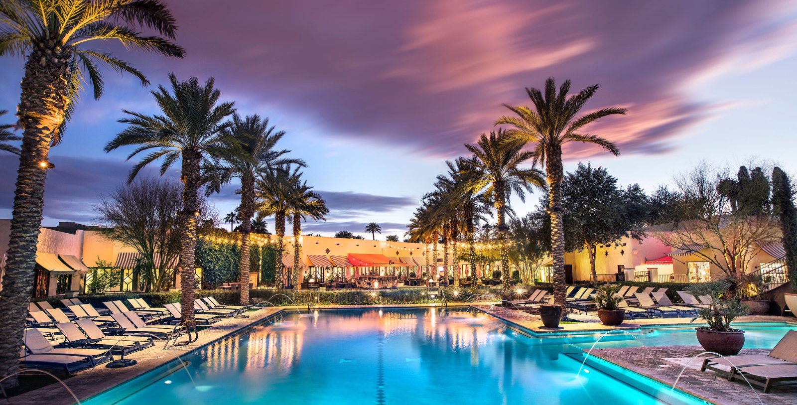 a pool with palm trees and a building with a pink sky