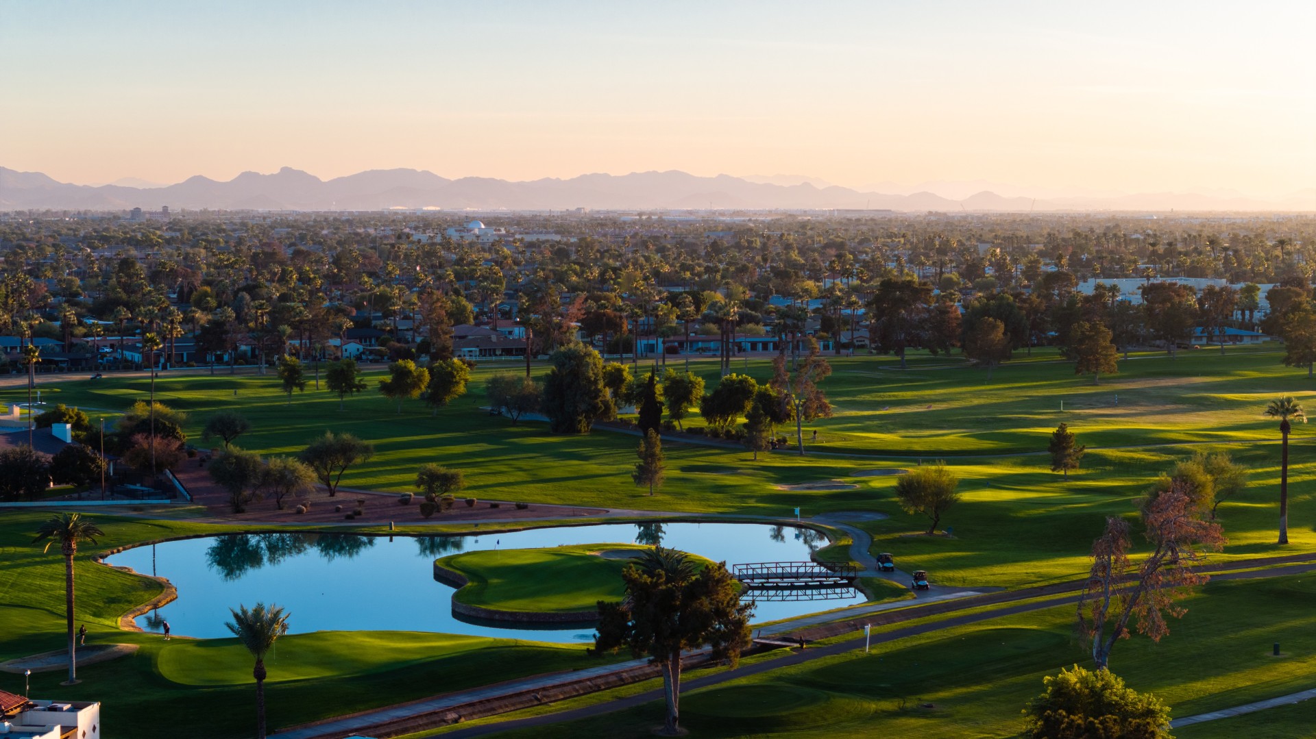 a golf course with a pond and a city in the background