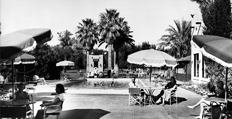 people sitting at tables and umbrellas by a pool