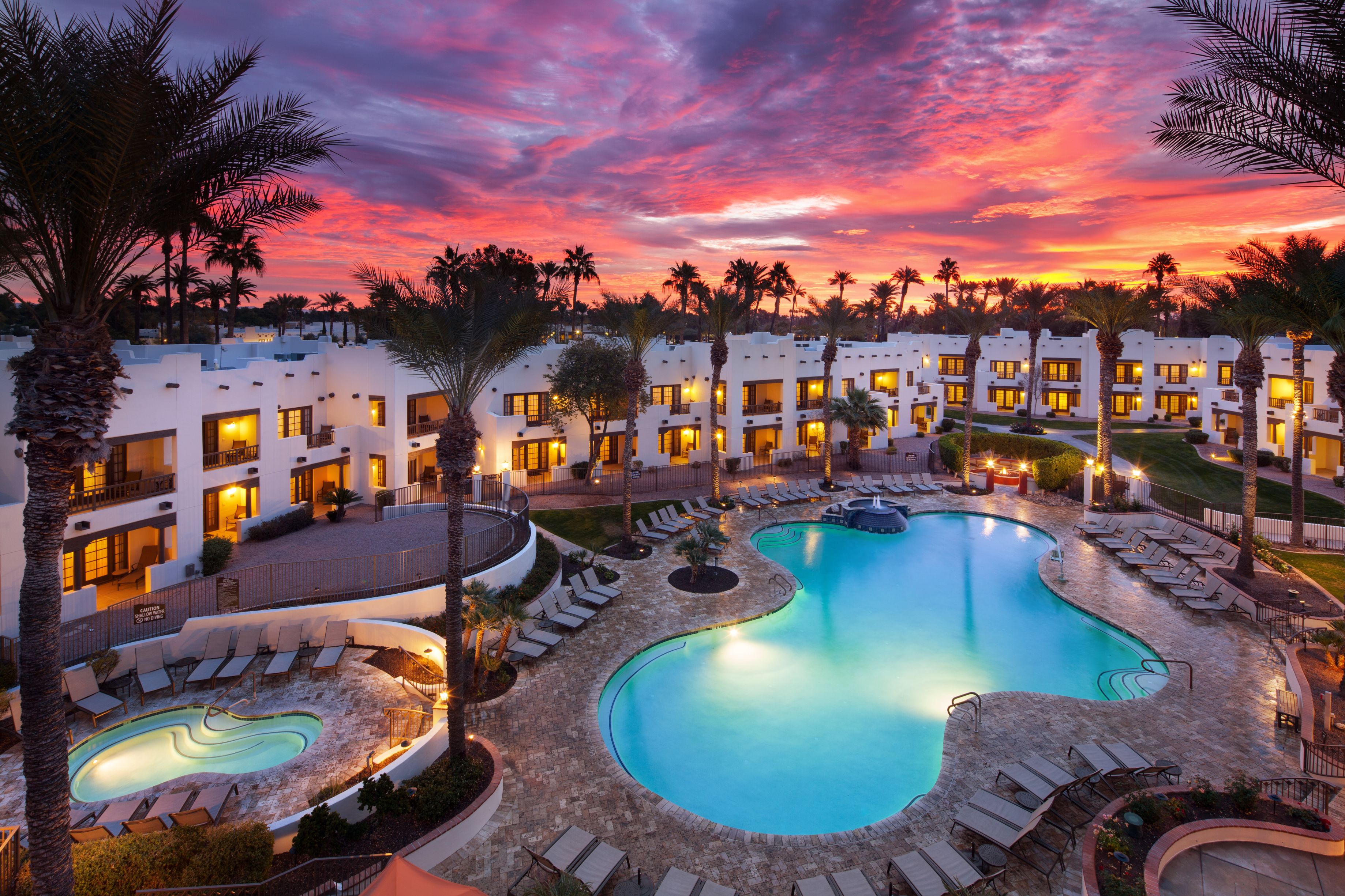 a pool and palm trees in front of a hotel