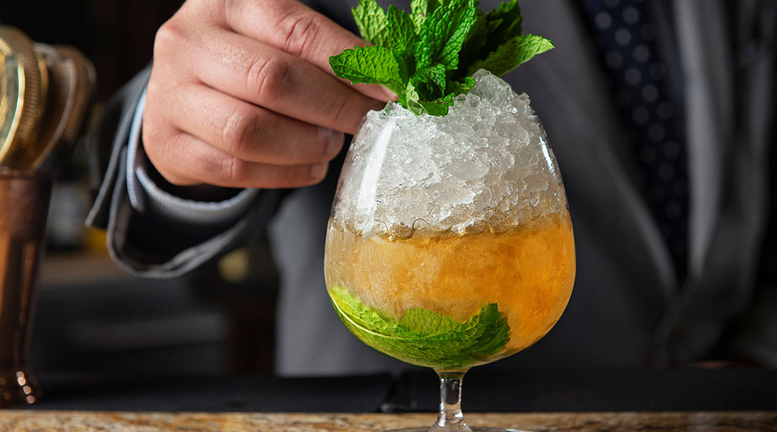 a hand holding a glass with a drink and a leaf of mint