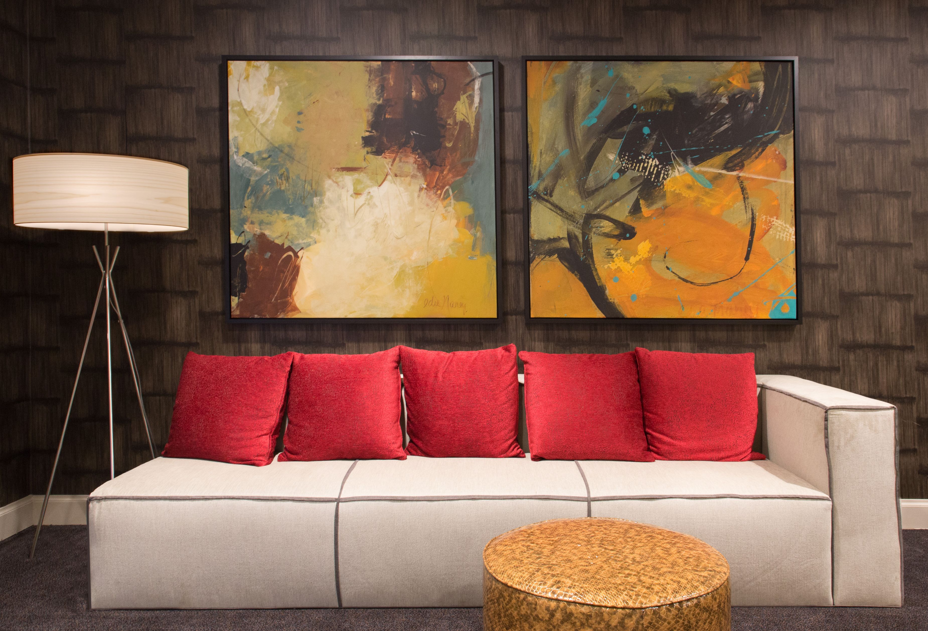 a couch with red pillows and a lamp in front of a painting