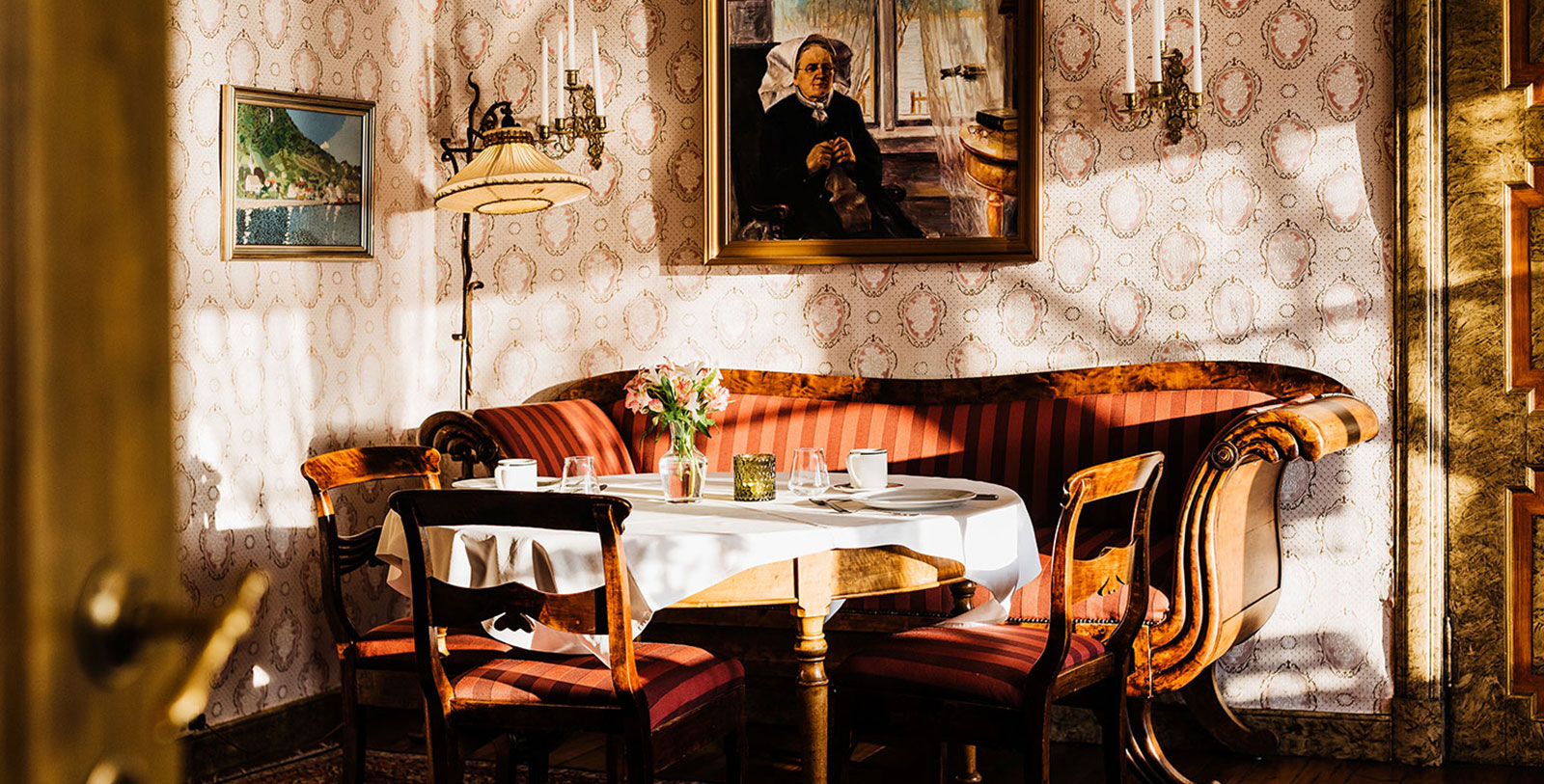 a table with a white tablecloth and chairs in a room with a painting on the wall