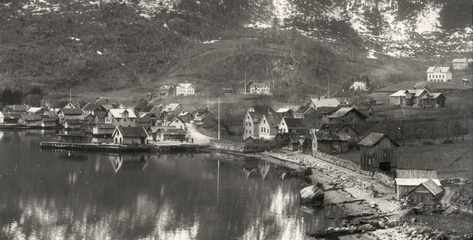 a black and white photo of a village next to a lake