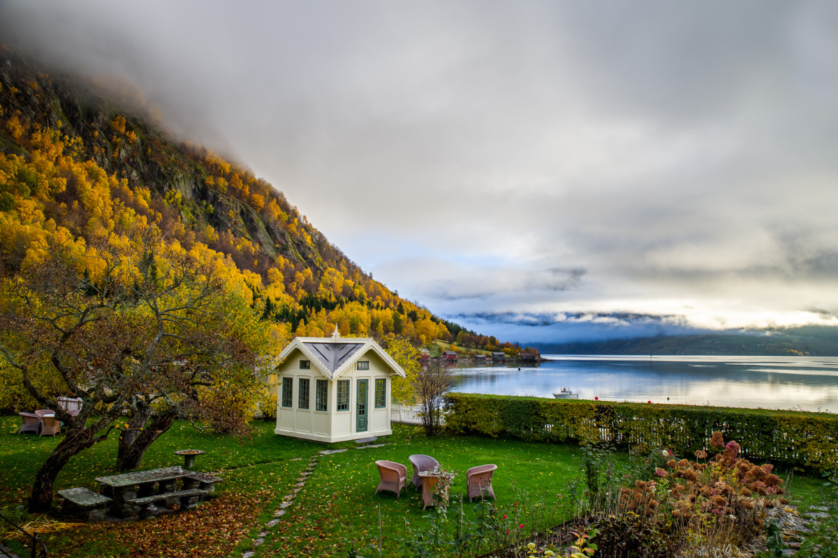 a small white house with chairs and a table in front of a body of water