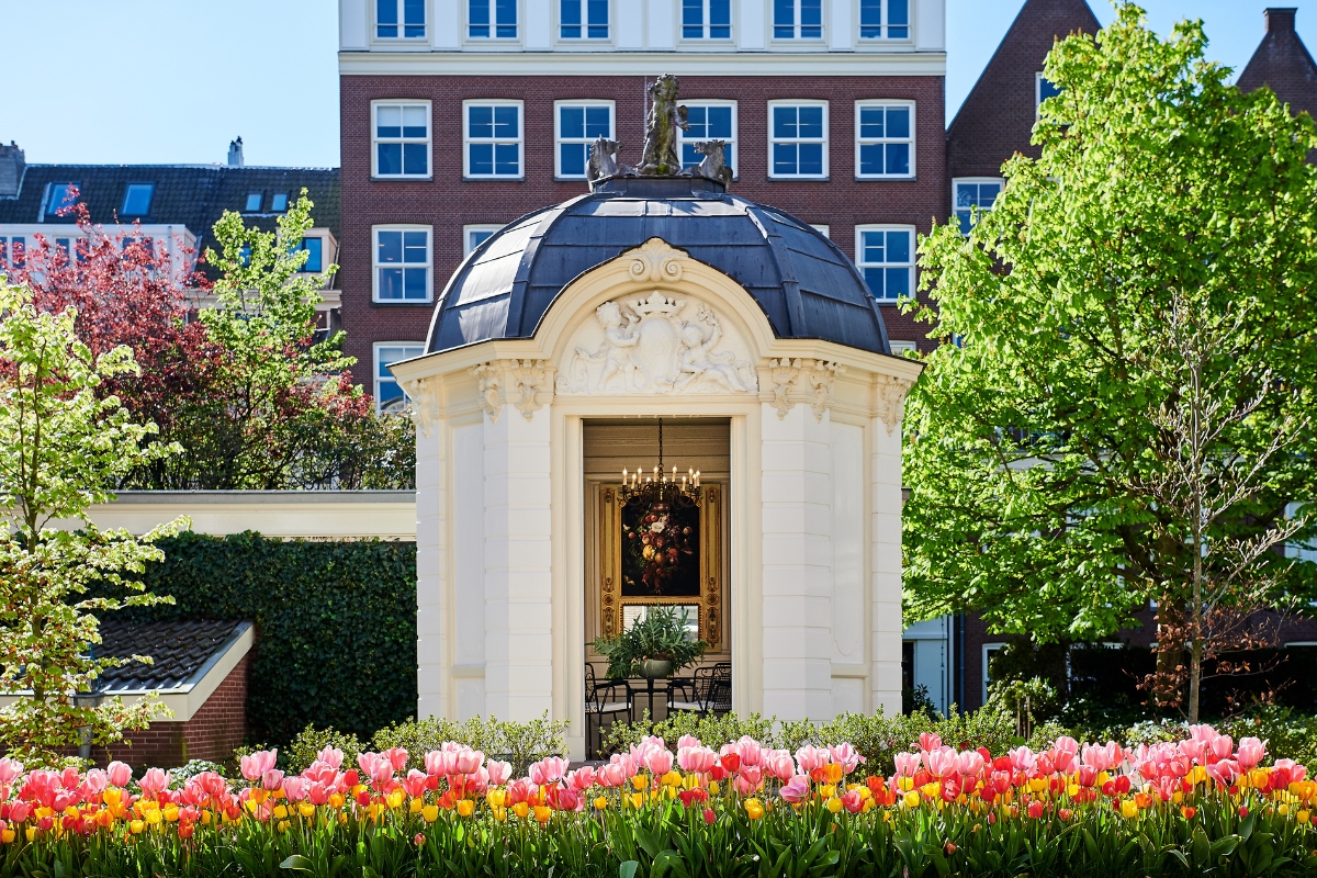 a small white building with a dome roof and flowers in front of it