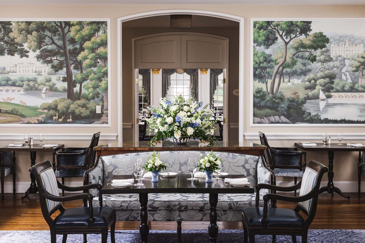 a table with flowers in front of a wall with a painting on the wall