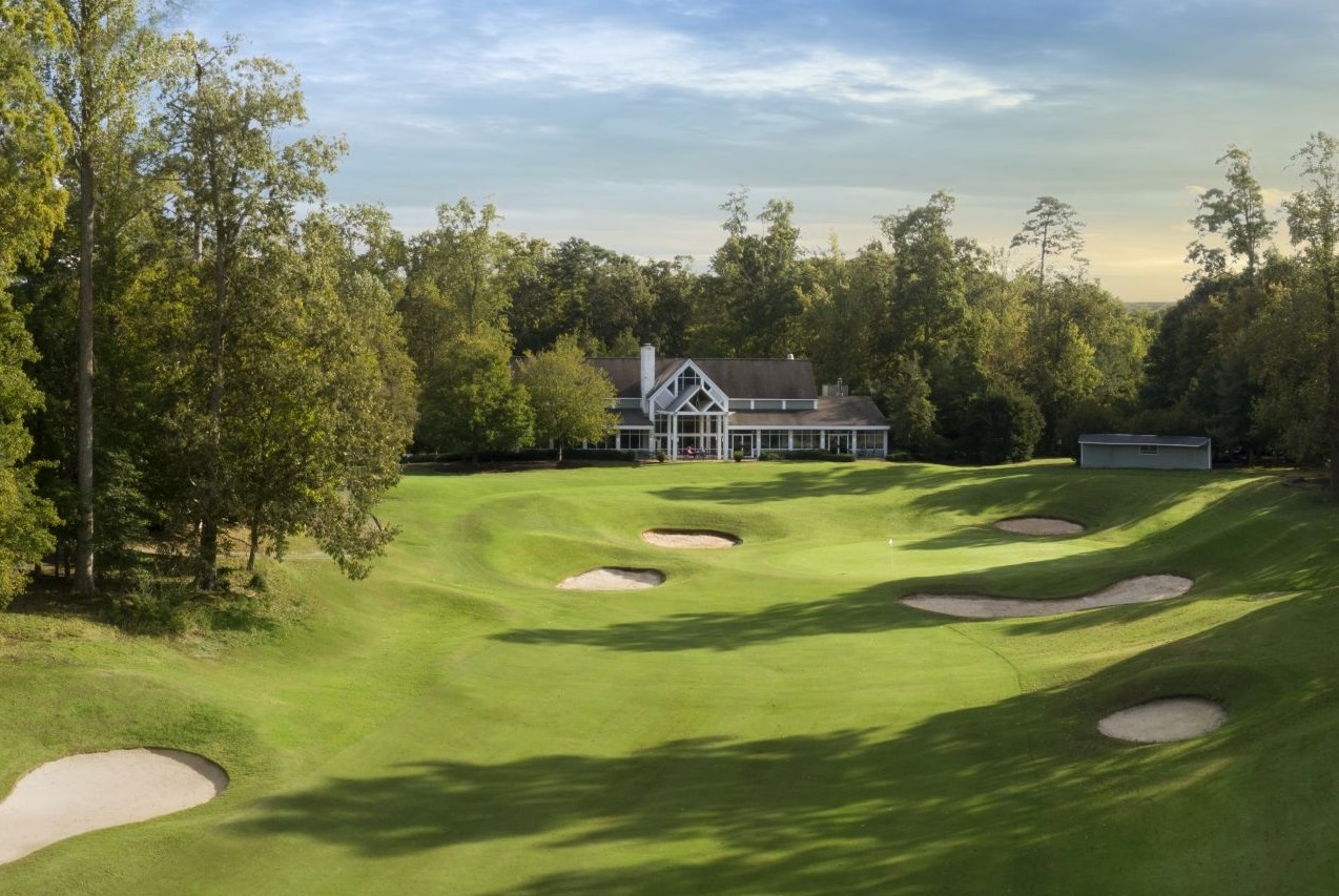 a large green golf course with a house and trees