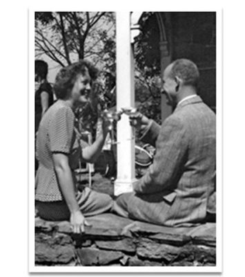 a man and woman sitting on a stone wall drinking from a glass