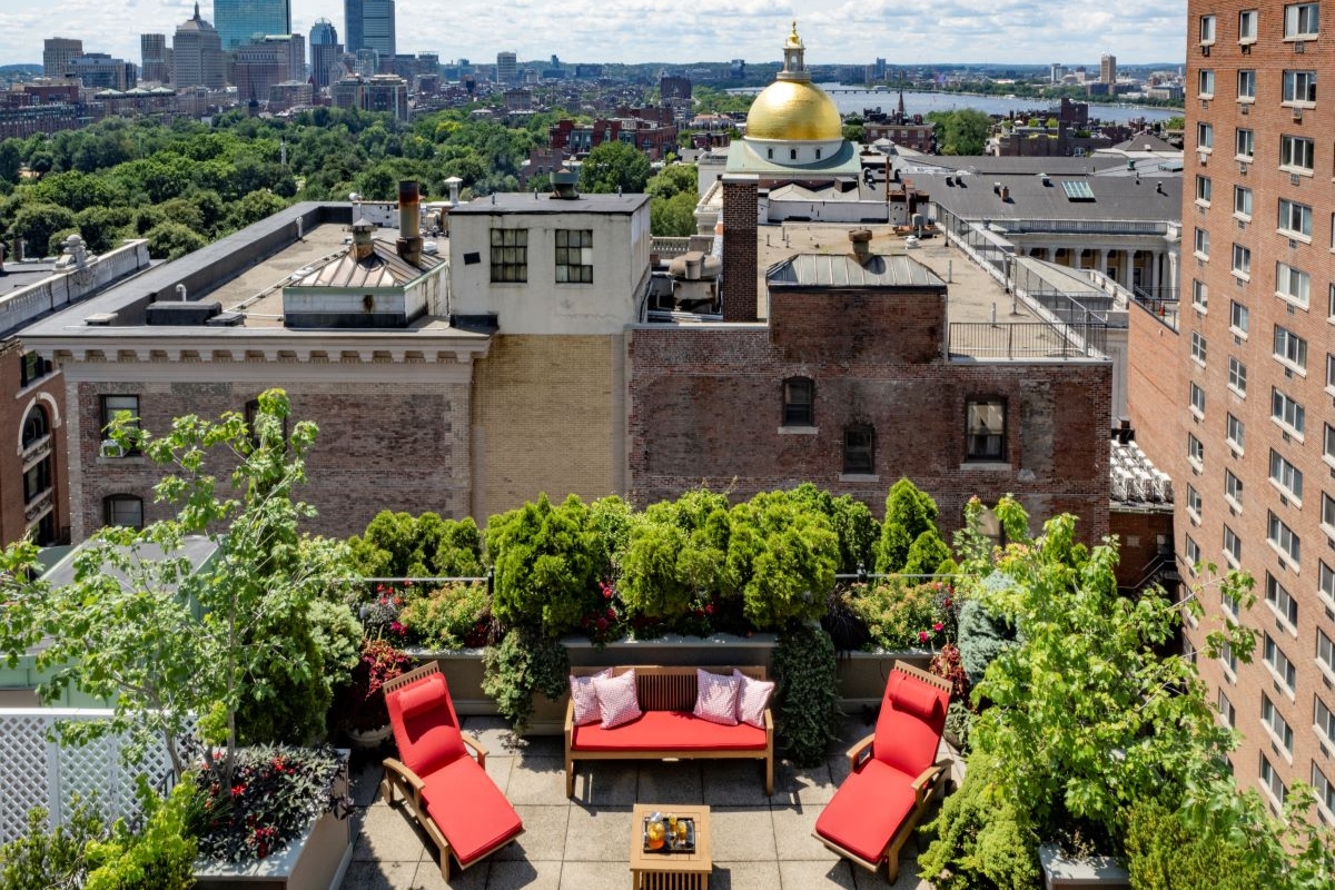 a rooftop patio with red chairs and trees and a city in the background
