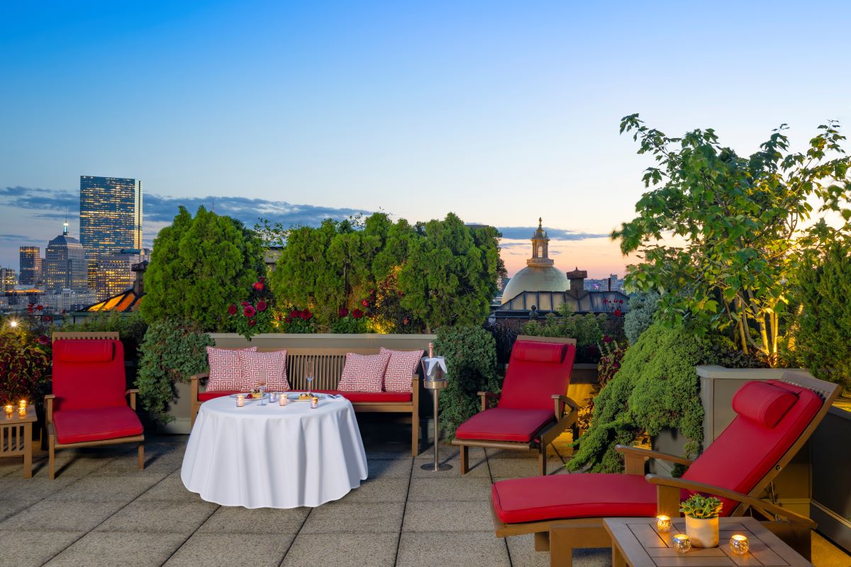 a table with a white tablecloth and red chairs on a rooftop